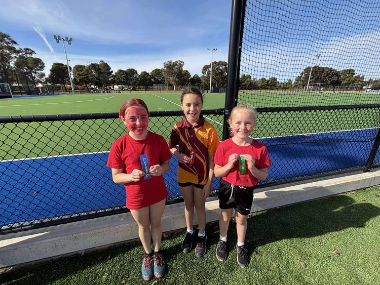 3 students dressed in red to support their team, holding placement ribbons